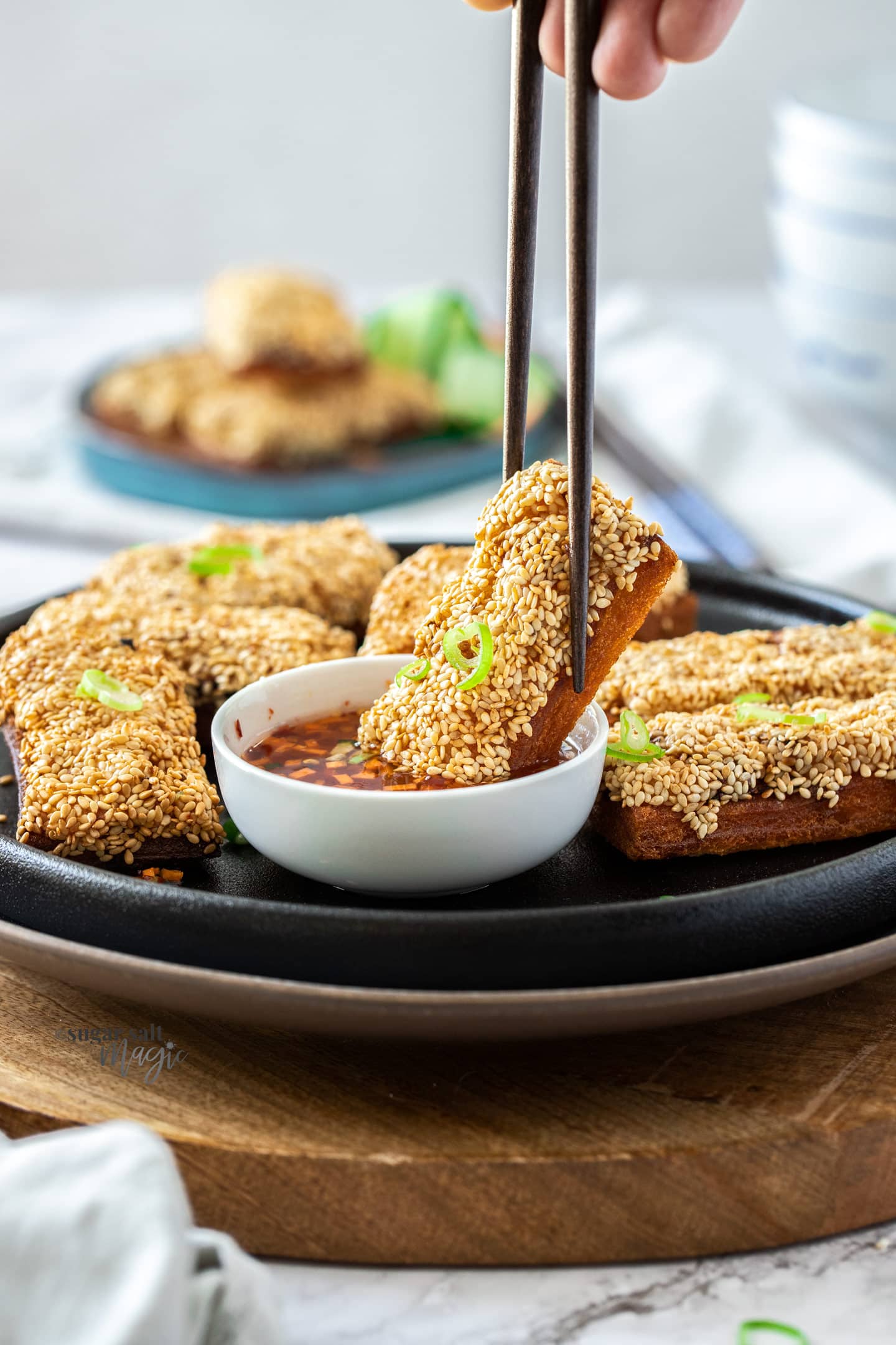 A slice of prawn toast being dipped into chilli sauce.