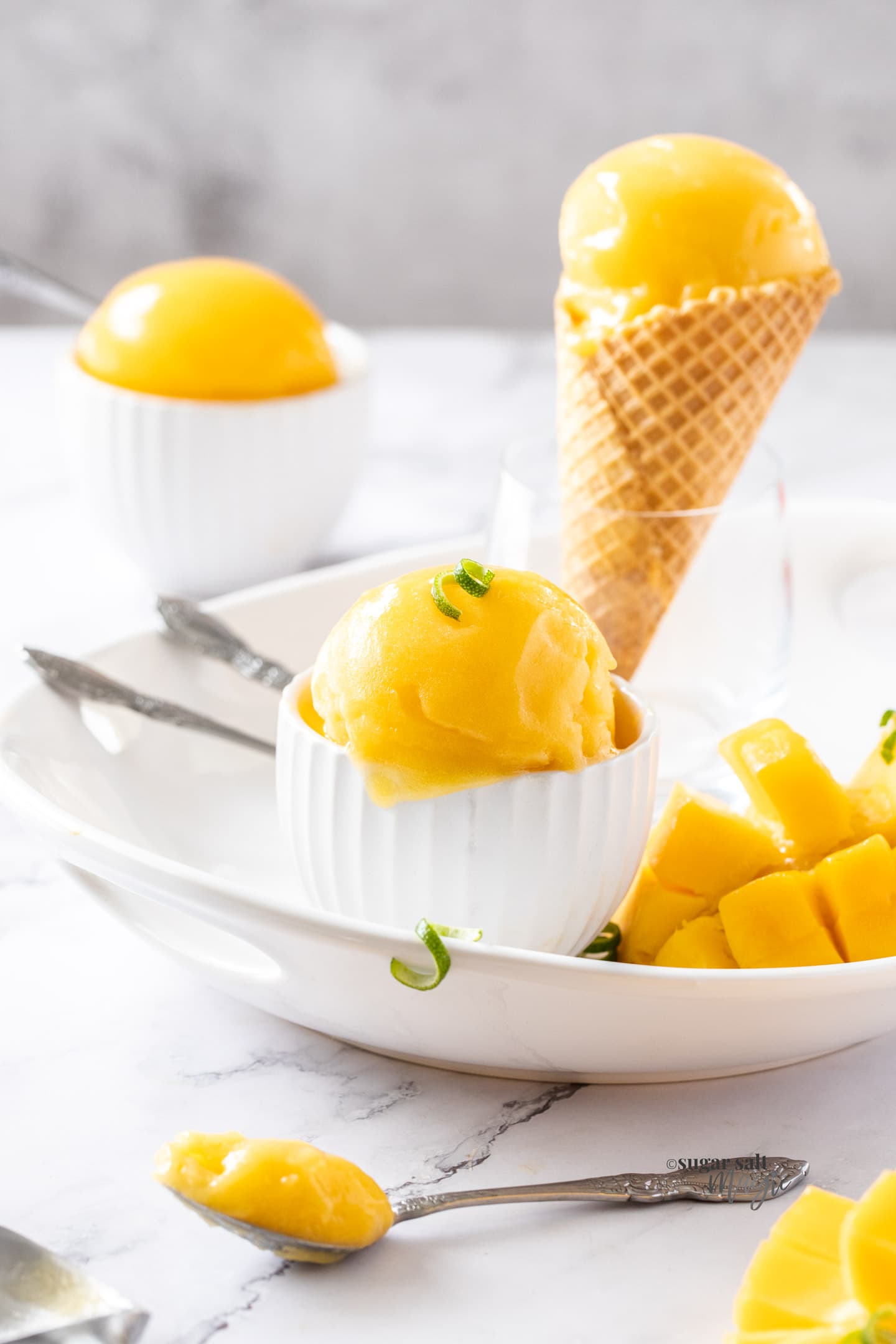 A white bowl with a big scoop of mango sorbet, a waffle cone in the background.