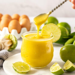 A spoon hovering over a glass jar filled with lime curd