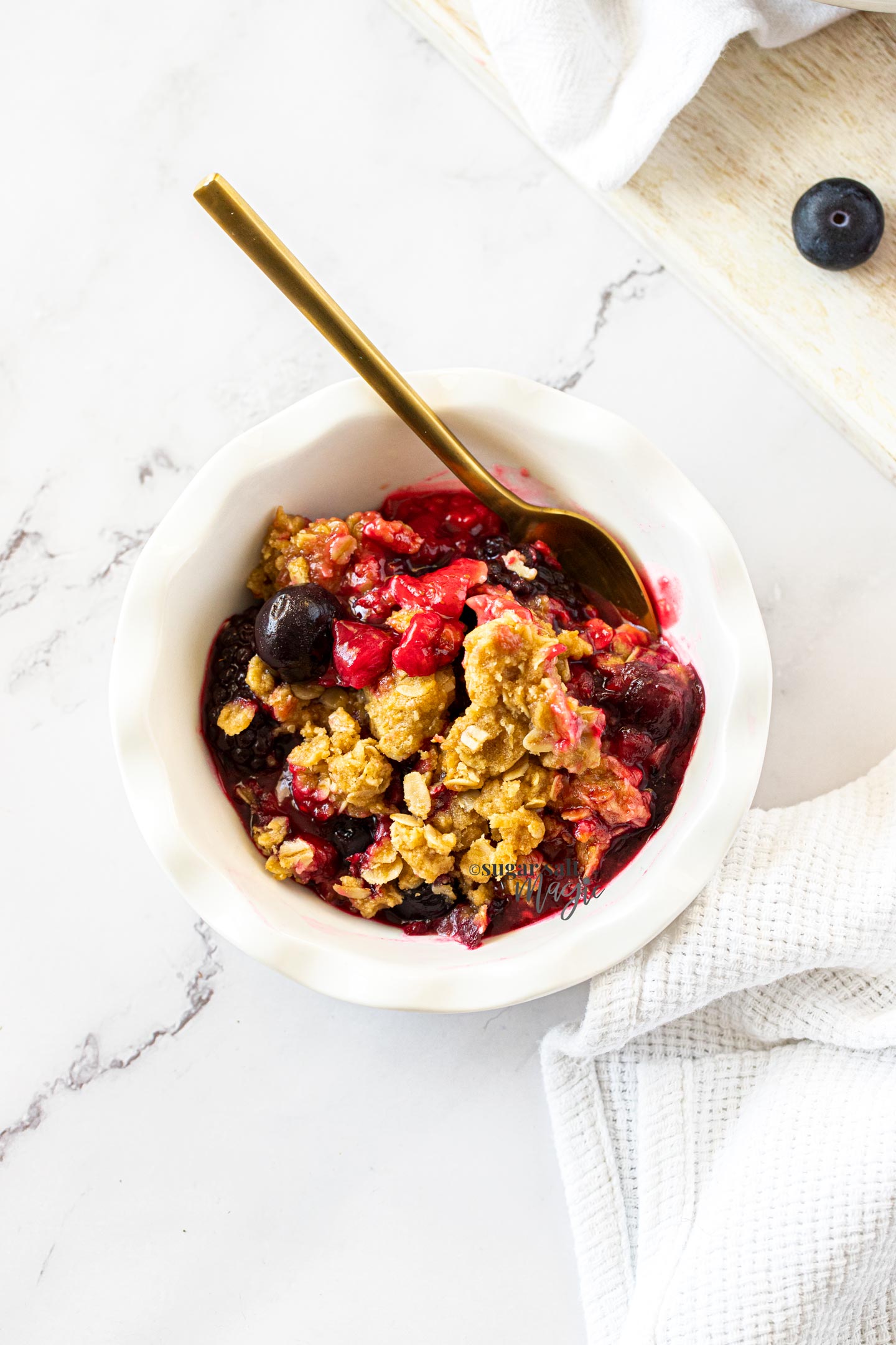 crumble and berries in a miniature white pie dish with a gold spoon
