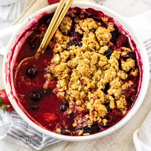 Top down view of a mixed berry crumble with gold spoons in it.