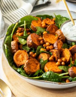A white bowl filled with spinach and sweet potato on a wooden board