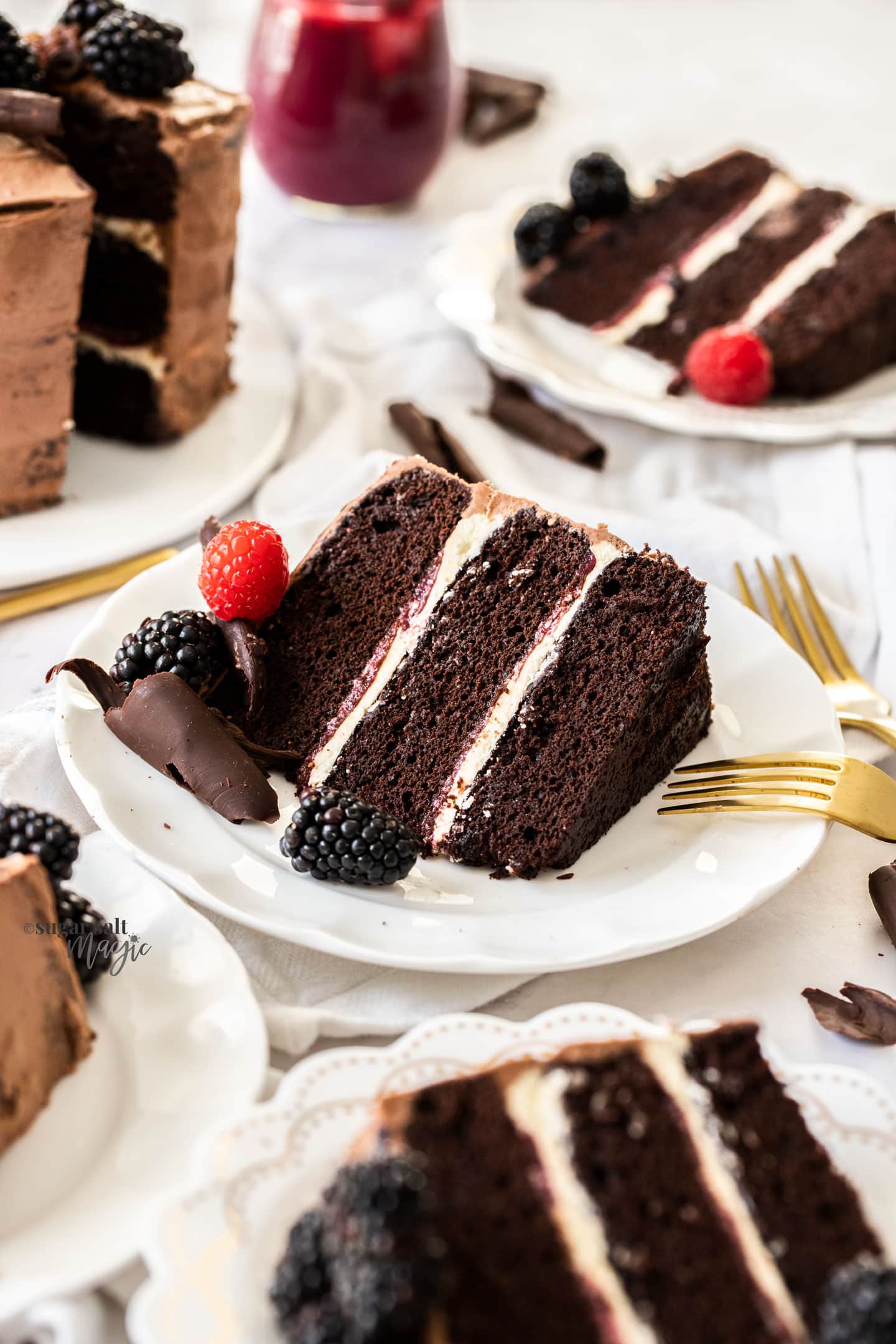 A slice of 3 layer chocolate cake on a white plate with more around
