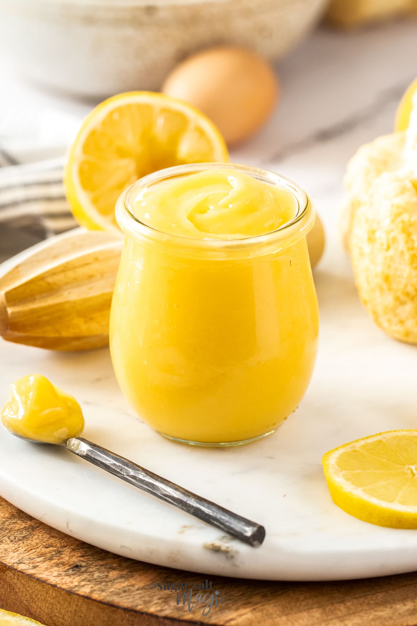 A glass jar filled with lemon curd with a spoon sitting next to it.