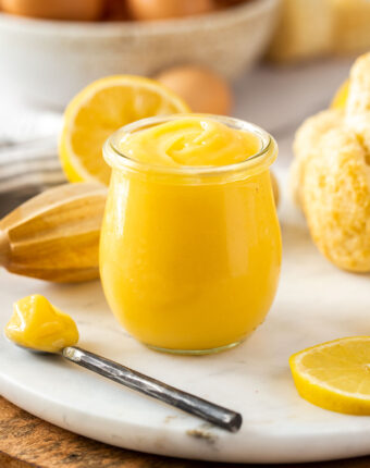 A glass jar filled with lemon curd with a spoon sitting next to it