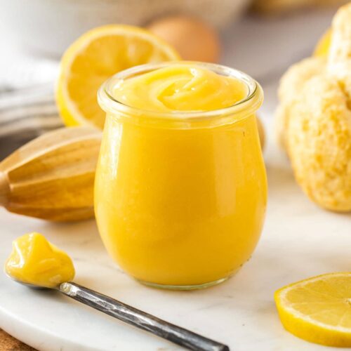 A glass jar filled with lemon curd with a spoon sitting next to it