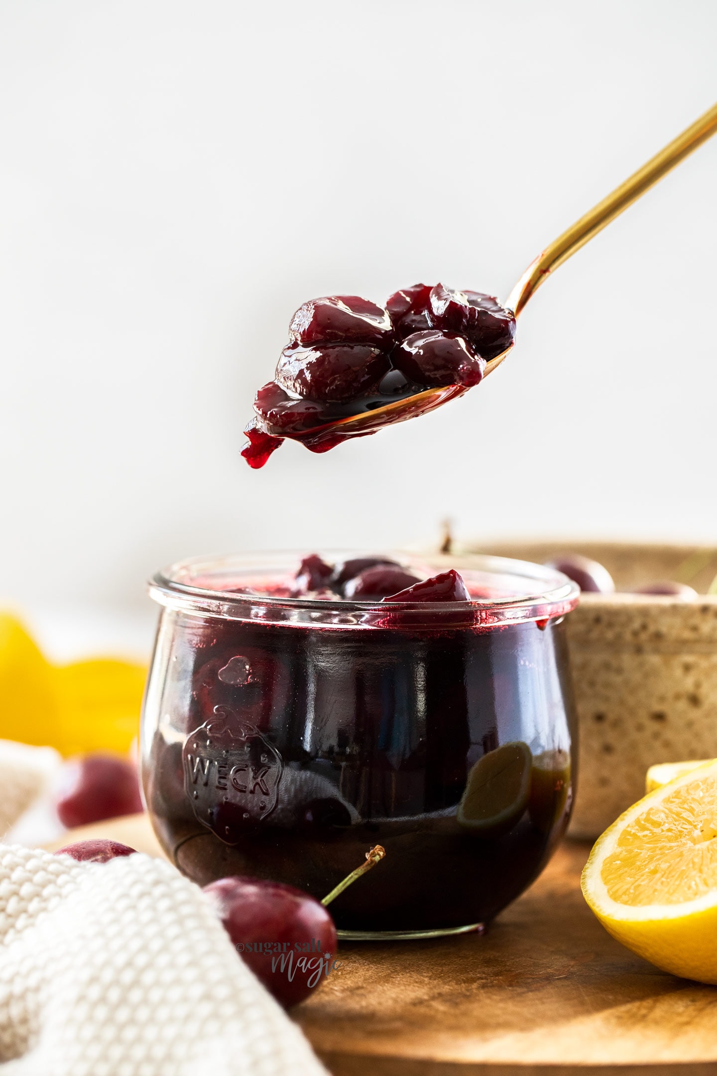 A gold spoon filled with cherry compote hovering over a jar full of it