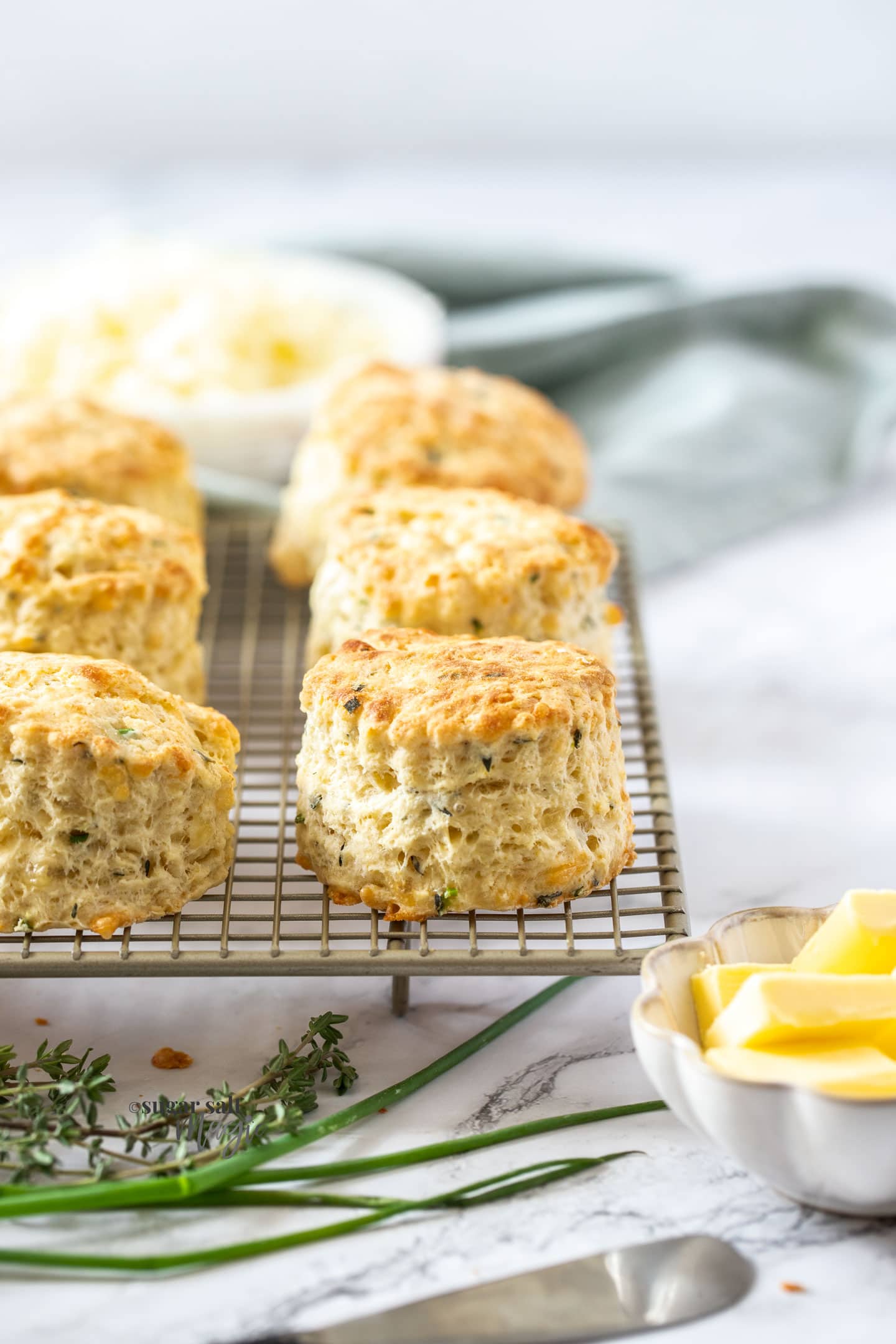 A batch of scones sitting on a wire rack with a bowl of butter next to them