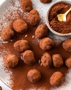 A batch of chocolate truffles on a plate with a small bowl of cocoa