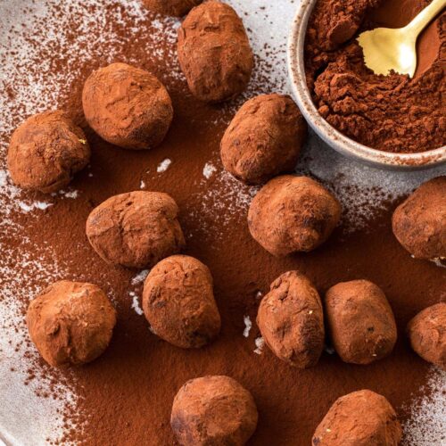 A batch of chocolate truffles on a plate with a small bowl of cocoa