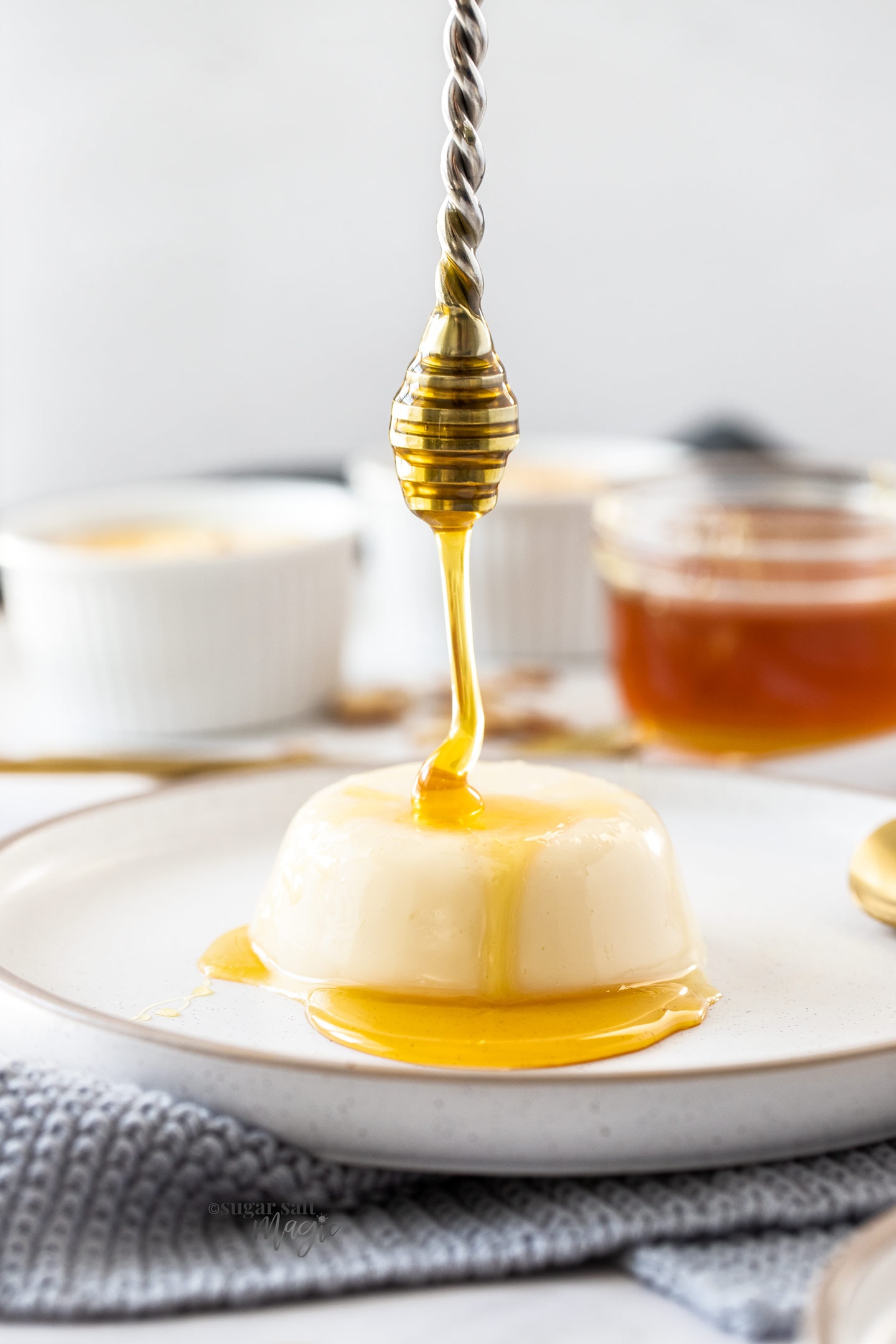 Honey being drizzled onto a panna cotta on a white plate.