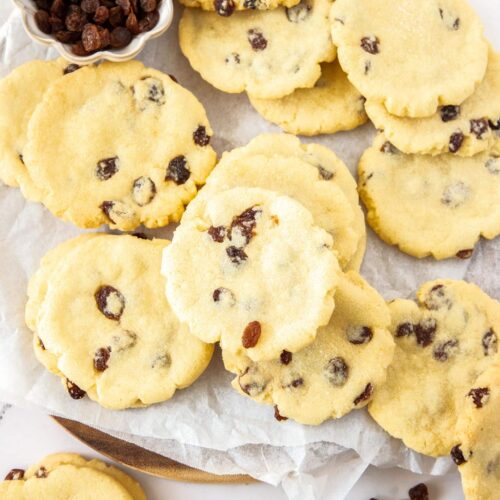 A pile of sultana filled cookies with a small bowl of sultanas.