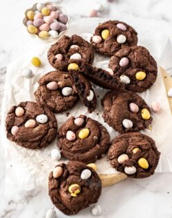 A batch of chocolate cookies on a wooden platter with mini eggs around.