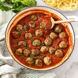 Meatballs in a pan of red pasta sauce with pasta in the background.