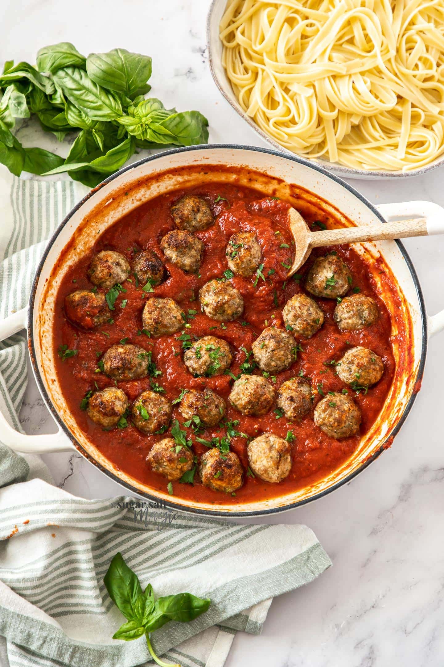 Meatballs in a pan of red pasta sauce with pasta in the background.