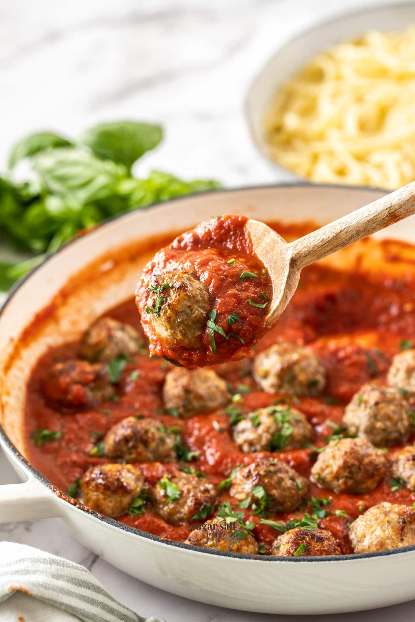 A meatball in red sauce on a wooden spoon.