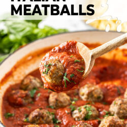 A meatball in red sauce on a wooden spoon.