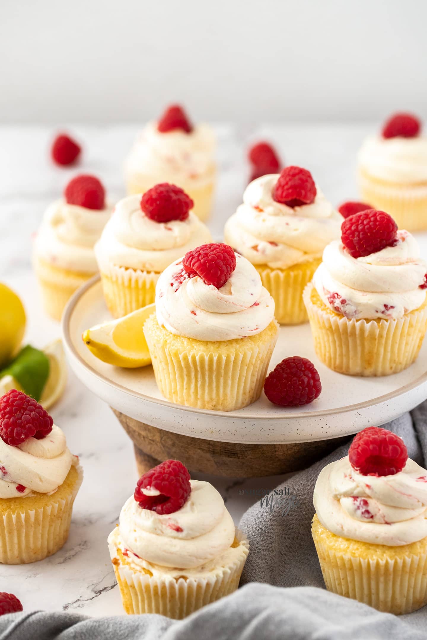 A batch of cupcakes topped with raspberries on a white plate.