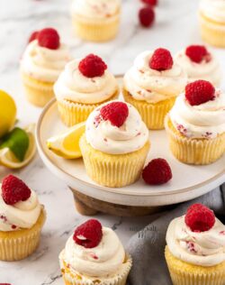 A batch of cupcakes topped with raspberries on a white plate.