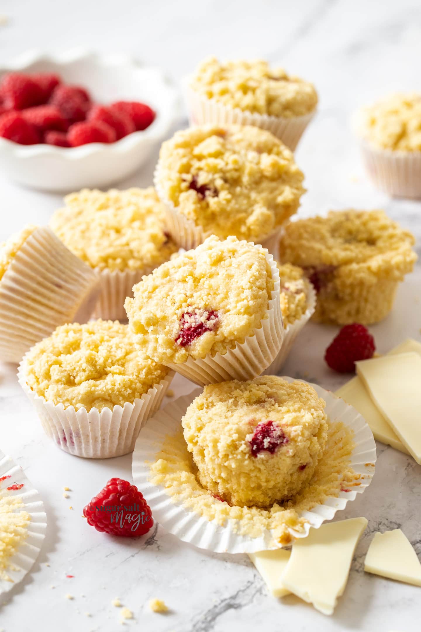 A batch of muffins with raspberries around them on a marble benchtop.