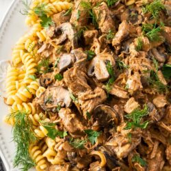 A white dish filled with pasta and beef stroganoff.
