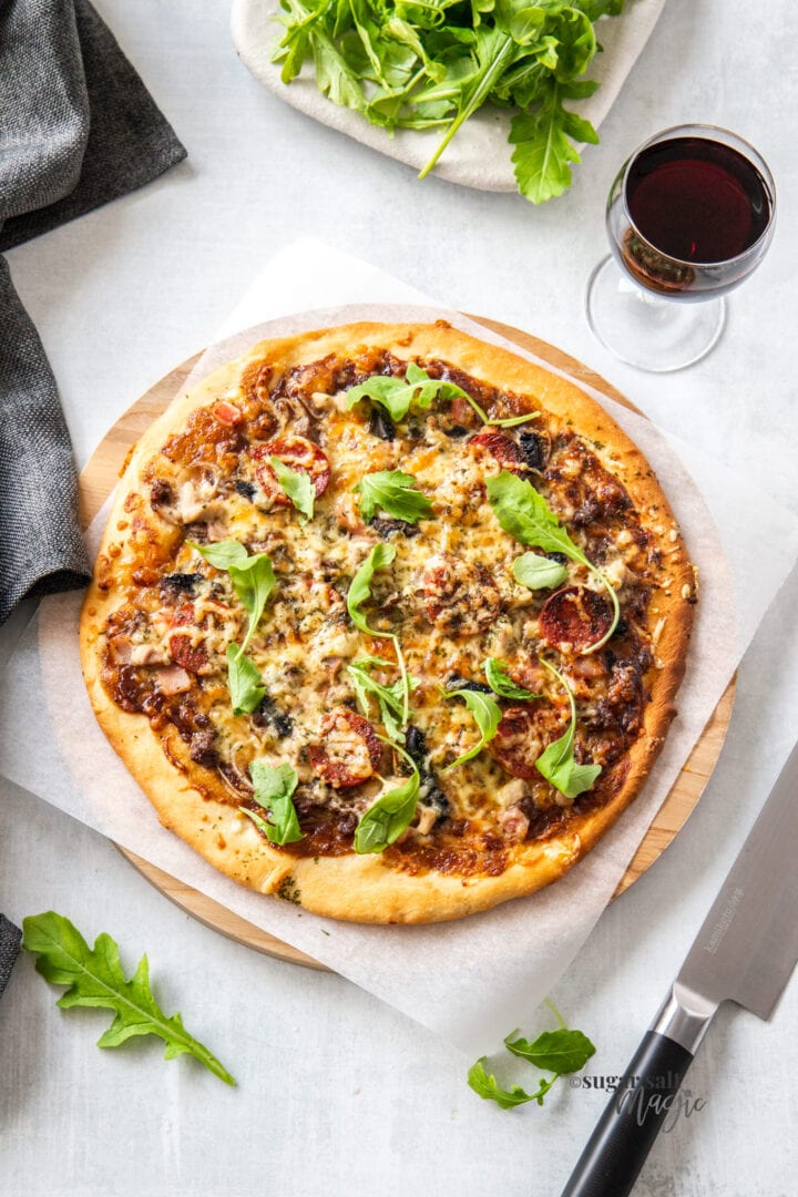 An unsliced pizza on a wooden board with a glass of wine nearby.