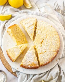 Top down view of a lemon ricotta cake cut into slices on a white platter.