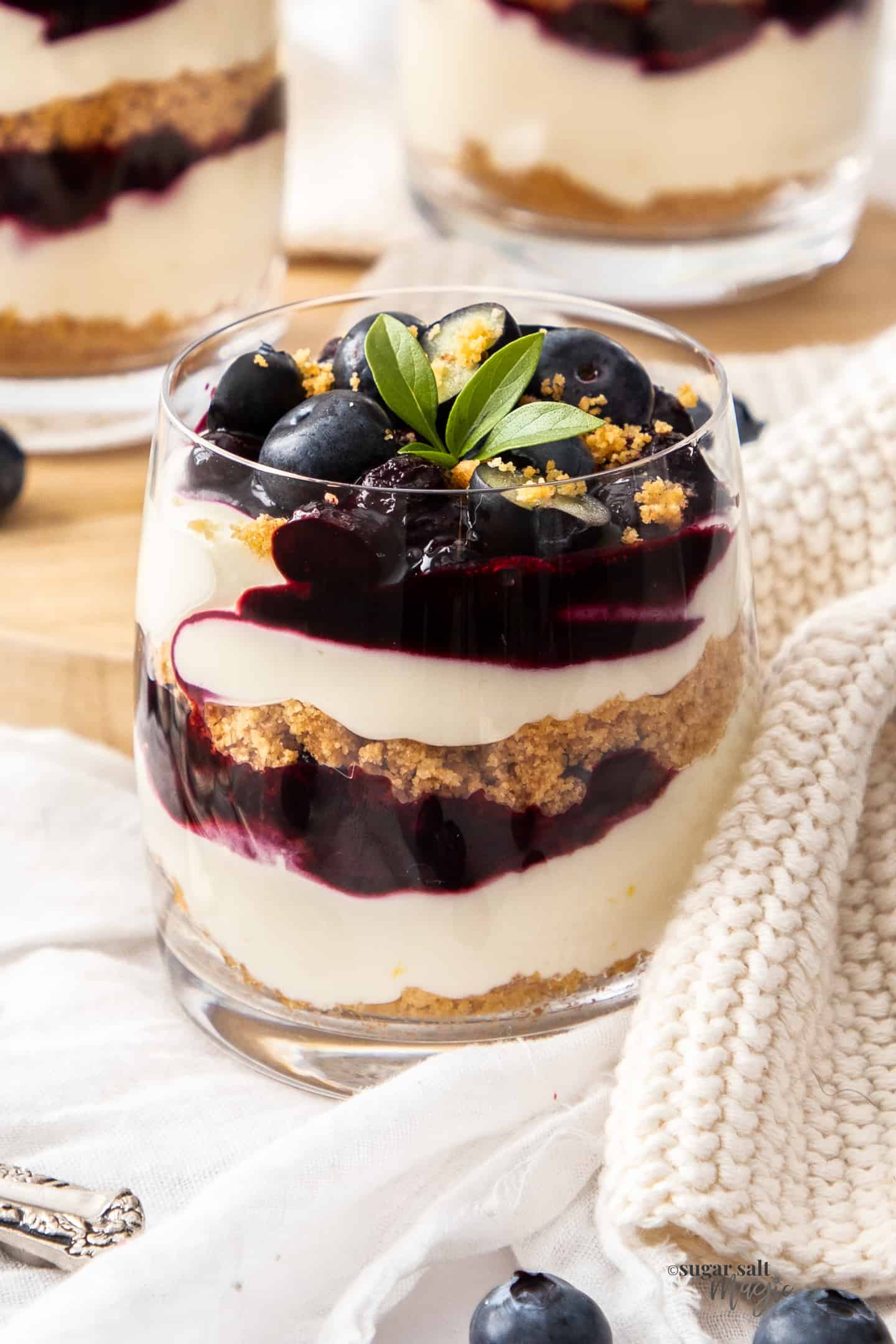 Closeup of a glass filled with layers of cheesecake and blueberry sauce.