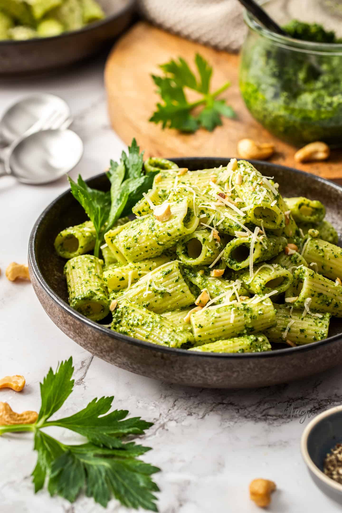 A dark brown bowl filled with pesto covered pasta.