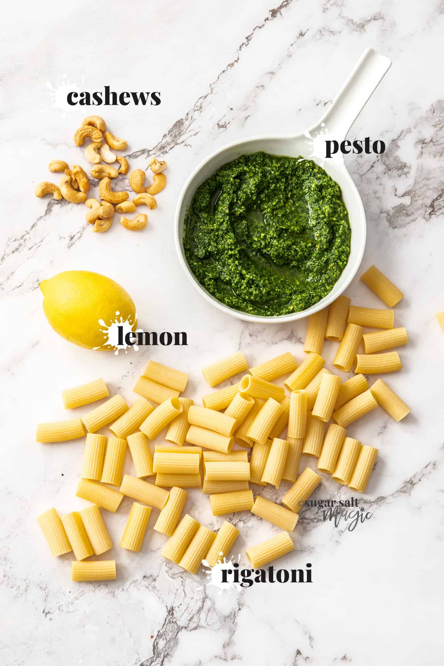 Ingredients for pesto rigatoni on a marble surface.