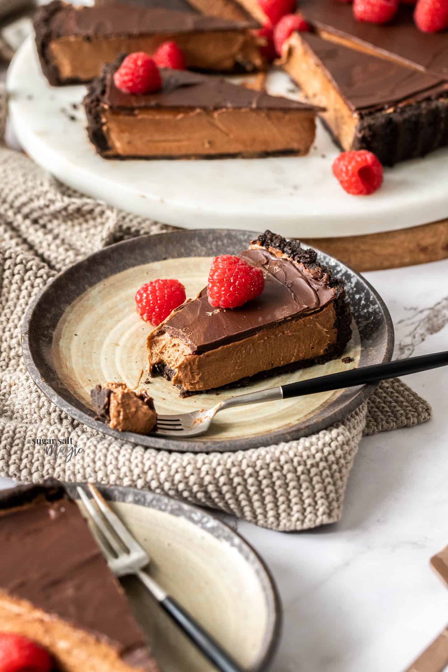 A slice of chocolate mousse tart on a brown cake plate with a bite taken out.