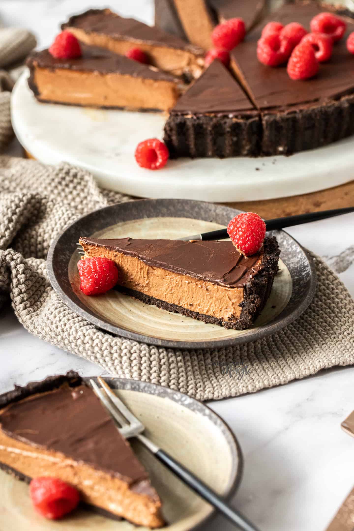 Slices ofchocolate mousse tart on brown cake plates, topped with raspberries.