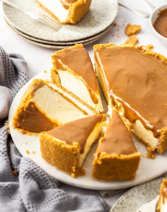 A cheesecake topped with dulce de leche cut into slices, on a white platter.