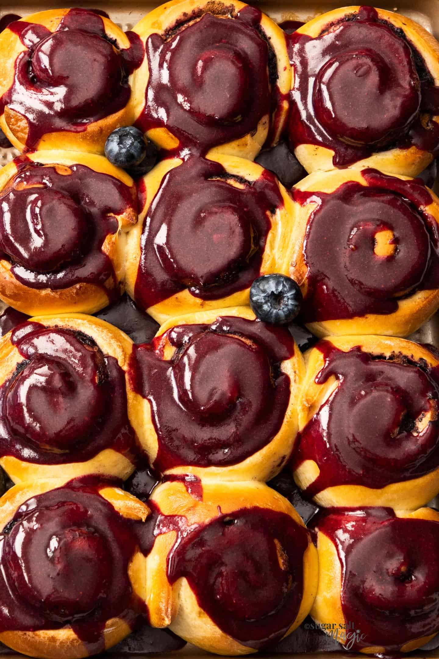 Top down, closeup view of 12 blueberry cinnamon rolls on a baking tray.