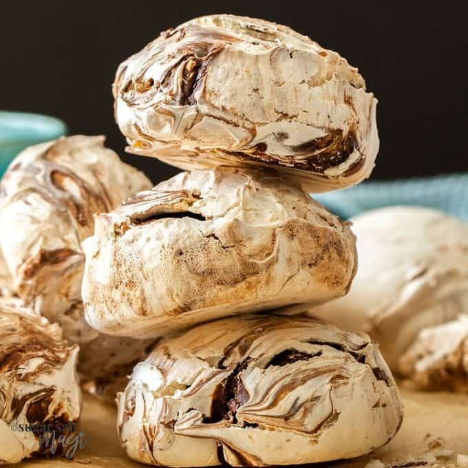 A stack of 3 large chocolate meringues on brown baking paper.