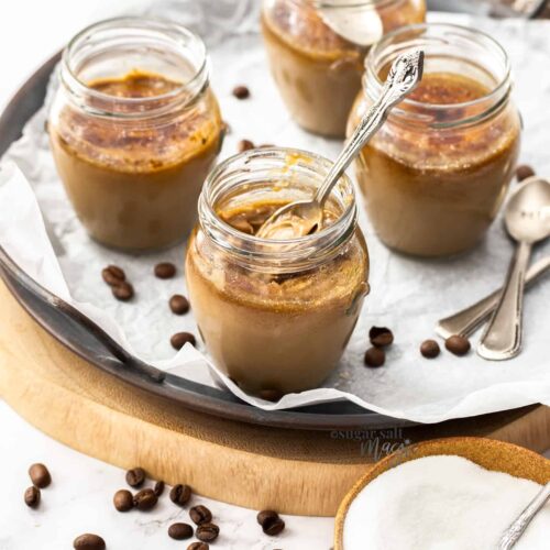 4 small jam jars filled with creme brulee with coffee beans scattered around.