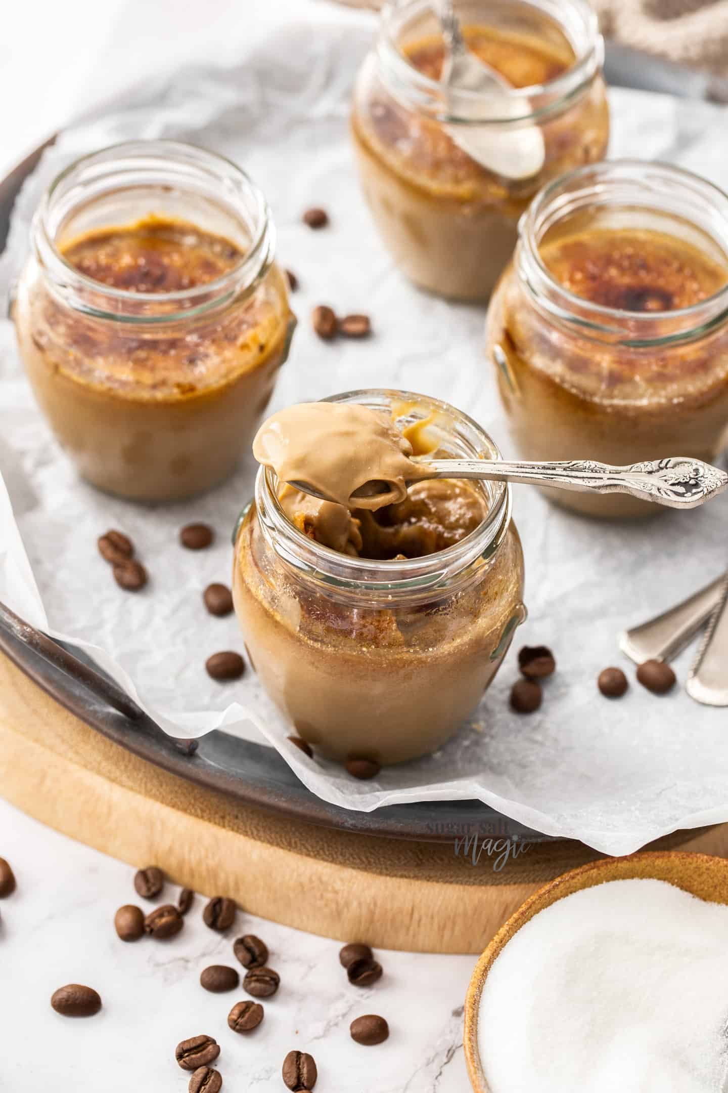 4 small glasses filled with coffee custard with a spoonful sitting on top.