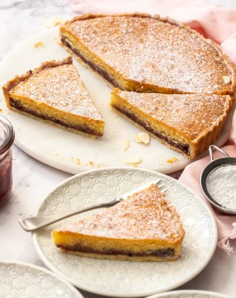 A bakewell tart cut into slices on a white marble cake platter.