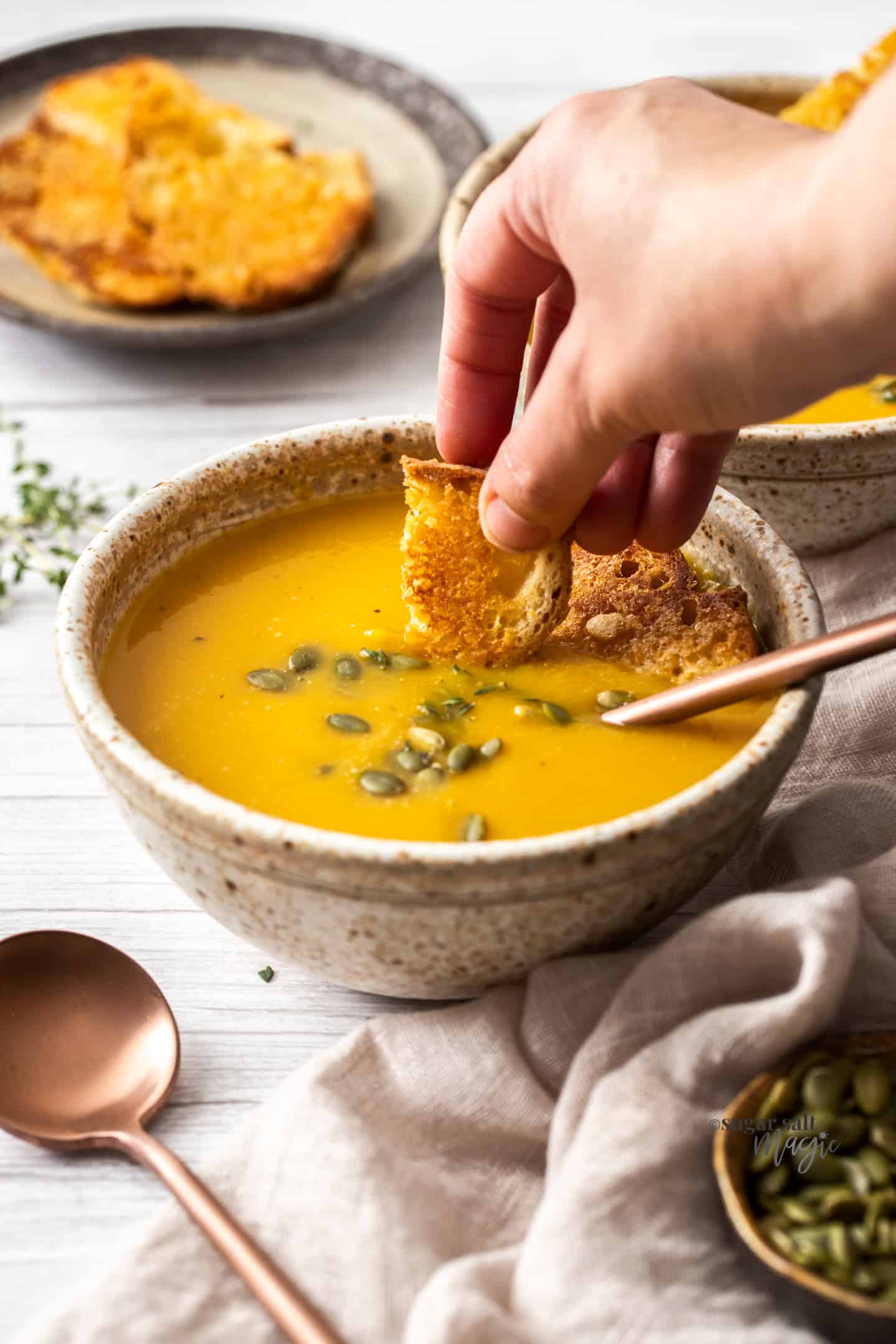 A hand dipping a piece of bread into a bowl of butternut soup.