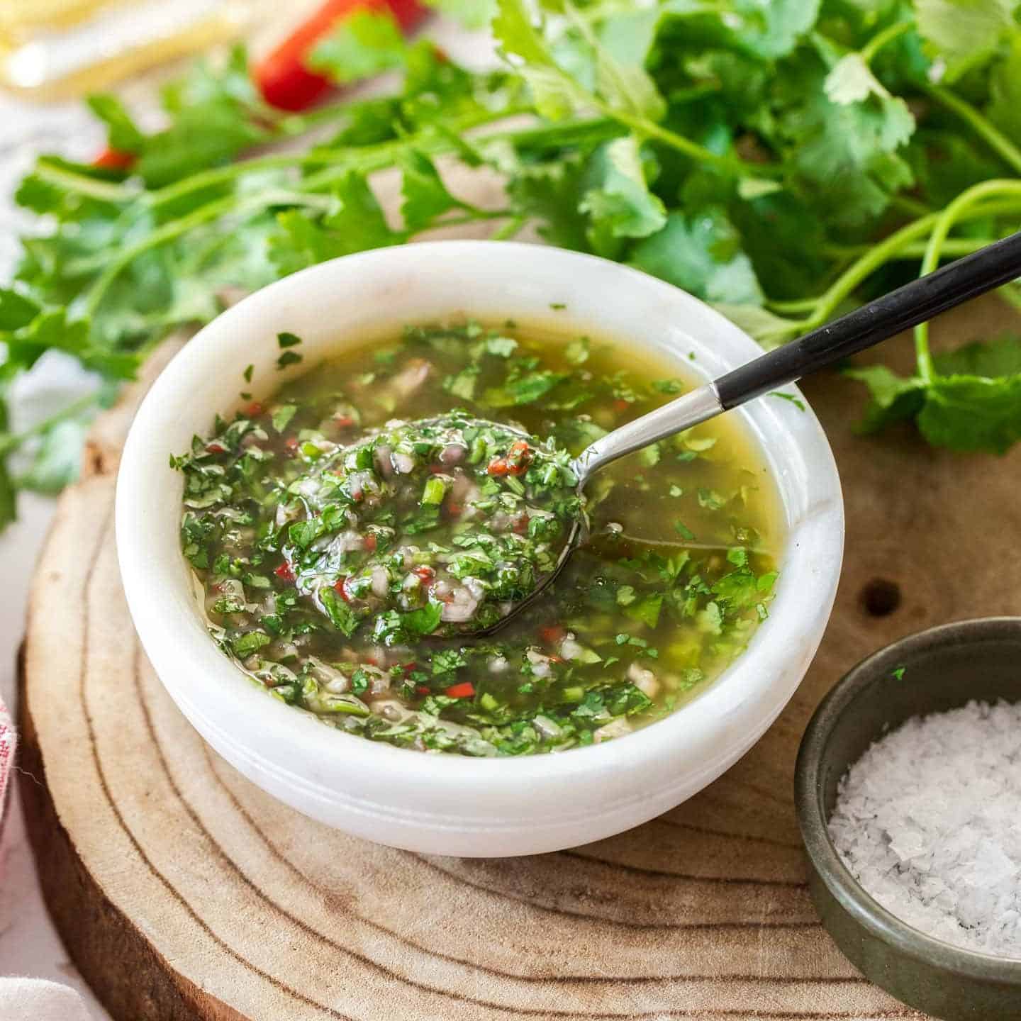 A bowl filled with herb sauce with a spoon dipping in