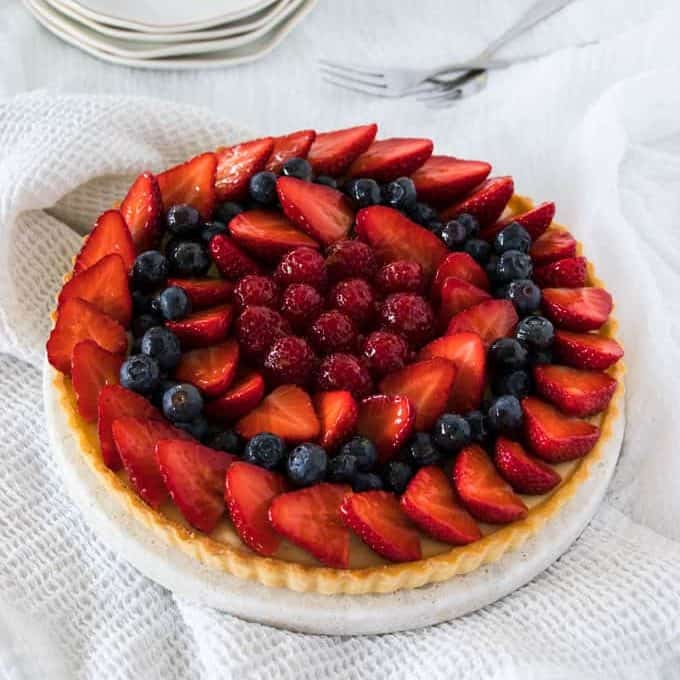 A tart topped with berries on a white cake plate.