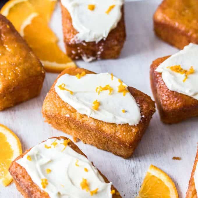 A batch of miniature orange loaf cakes surrounded by slices of orange.