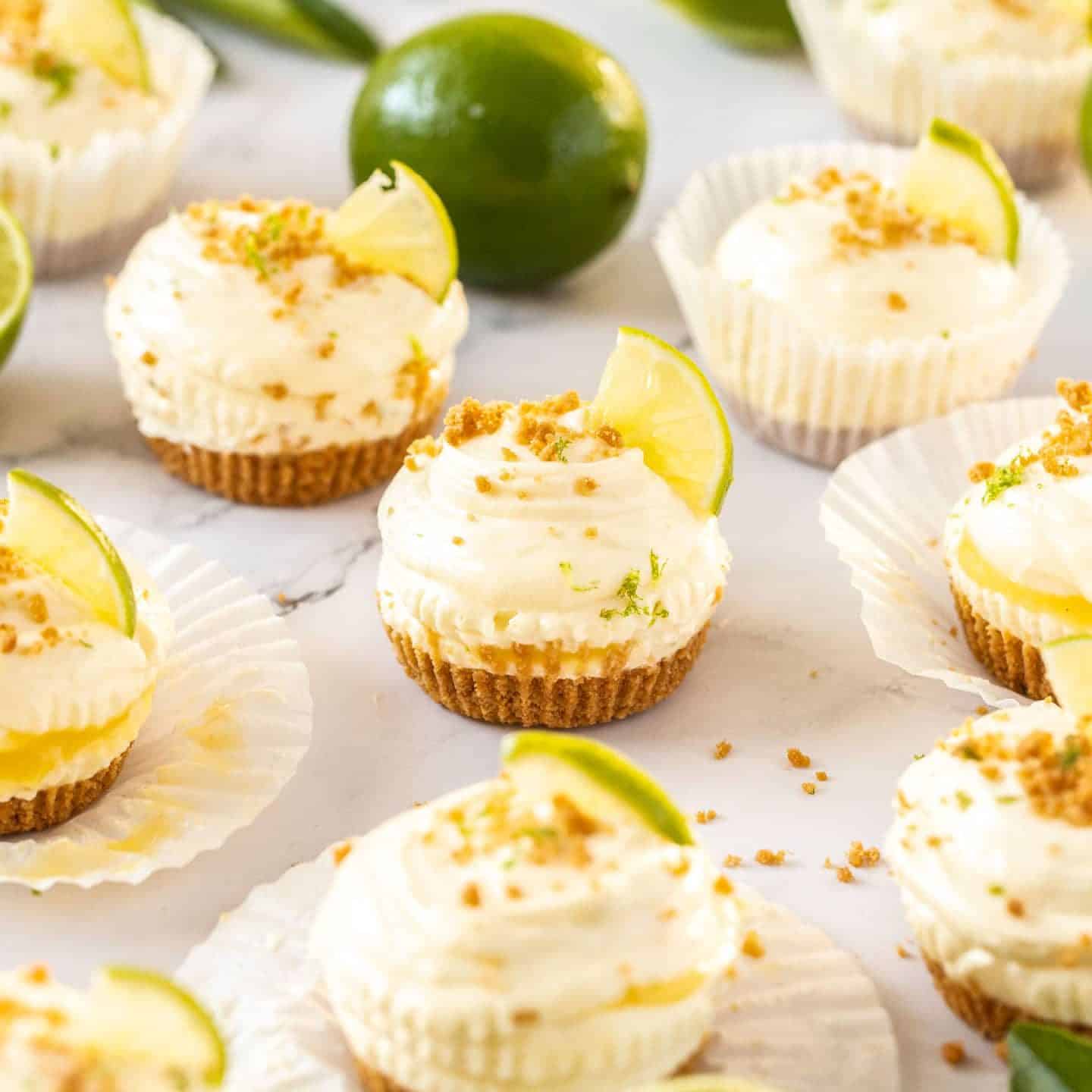 A batch of mini cheesecakes surrounded by limes and cookie crumbs