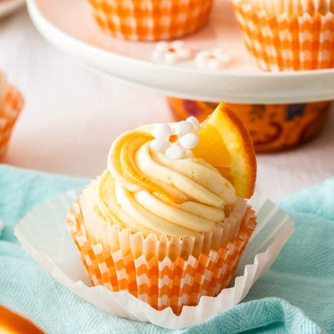 A closeup of an orange cupcake with white frosting.