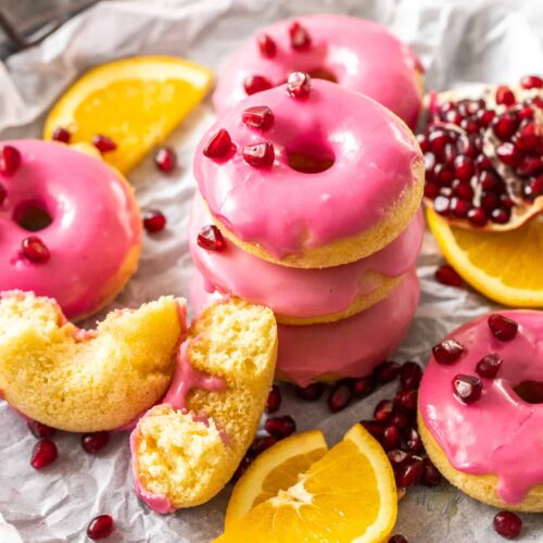 A stack of donuts with pink frosting surrounded by orange slices and pomegranate seeds.