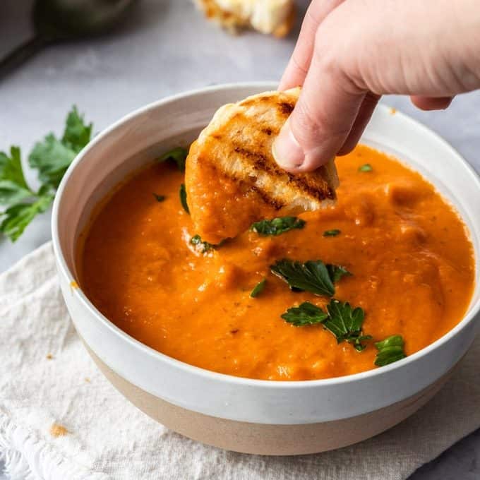 Dipping a grilled cheese sandwich into a bowl of tomato soup.