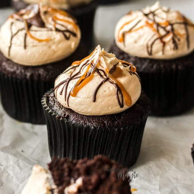 A chocolate cupcake in a black wrapper topped with caramel buttercream and streaks of caramel sauce.