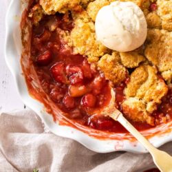 A white pie dish filled with strawberry rhubarb cobbler and a scoop of ice cream.