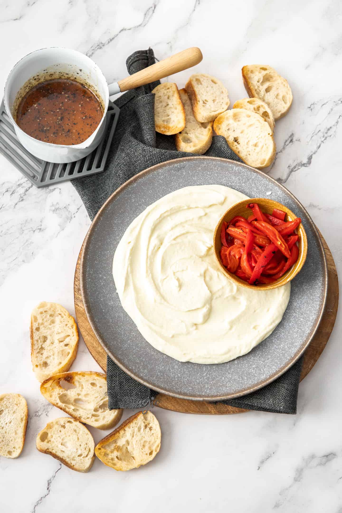Goats cheese spread over a large grey plate with a small bowl of roasted peppers next to it.