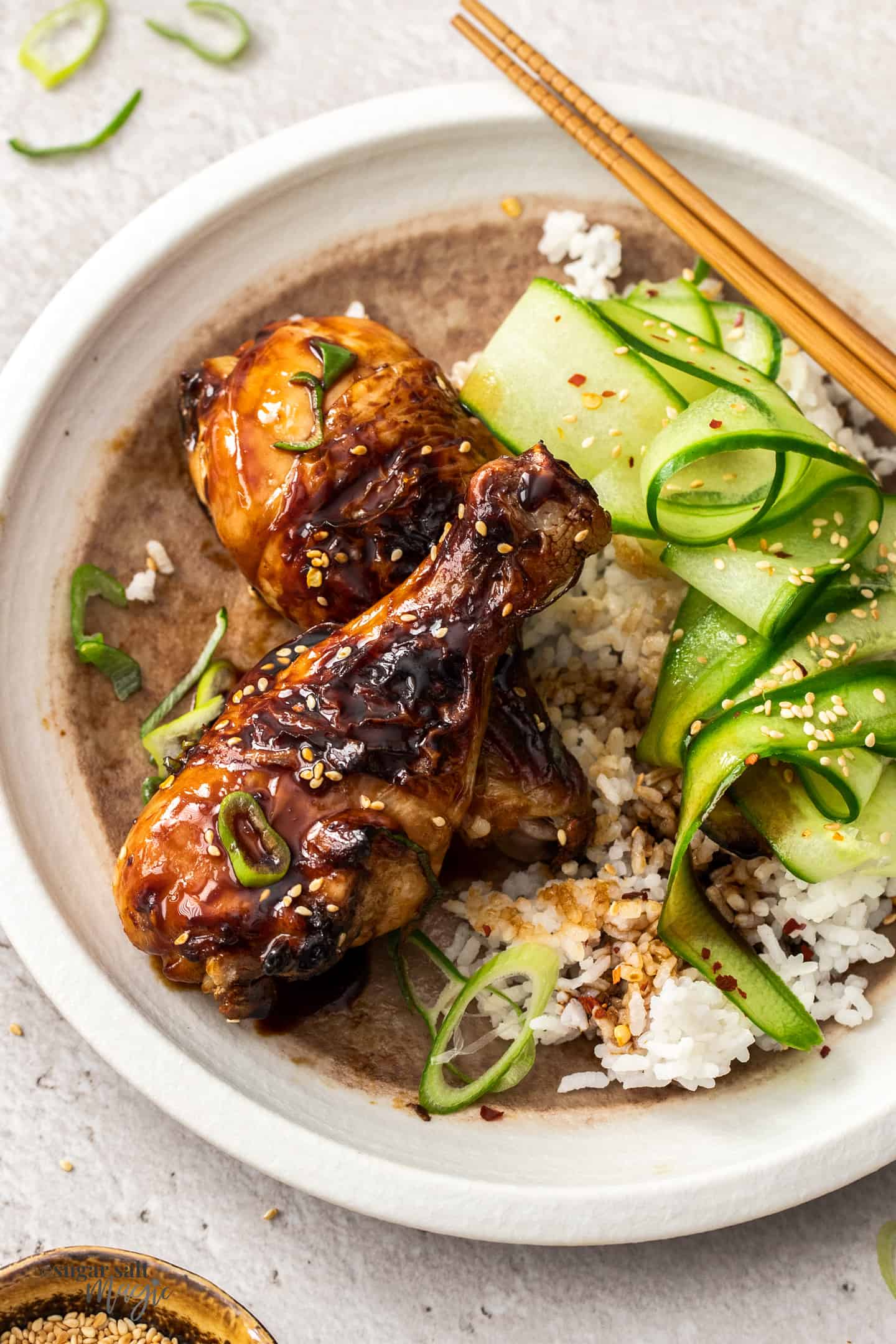 Two cooked chicken drumsticks on a white plate with rice and cucumber.